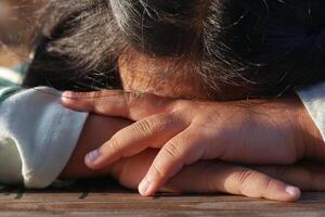 Child resting on table with hands folded at a sunny outdoor setting photo