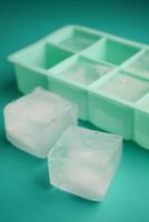 Ice cubes and tray on teal surface with two cubes separated photo