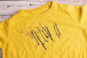 Yellow sweater with ink stains on wooden background photo