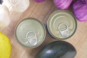 Canned food and fresh vegetables on a wooden surface in bright light photo