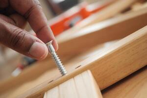 Person installing a screw into wooden material in a workshop photo
