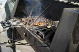 cooking meat on grill at barbecue party in summer garden. Food, people and family time concept. pork on skewers roasting on coals in large metal grill device. smoke from fire photo