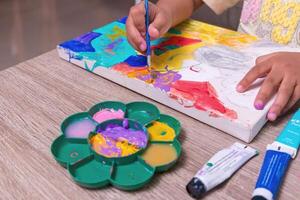 A little girl coloring on a canvas using watercolors on a table photo