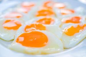 Close up of multiple sunny-side-up eggs with vibrant orange yolks and glossy whites, freshly cooked and arranged on a white plate, perfect for breakfast or food related concepts. photo