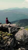 A woman sitting on top of a mountain looks into the distance at the beauty of the Carpathian mountains. Aerial view. Silhouette of a woman sitting on a rocky video