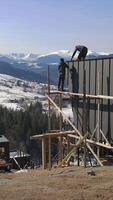 two men working on a building with snow covered mountains in the background video