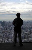 Silhouette of a man standing in front of a window with the skyline of Tokyo in the background photo