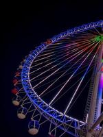 Bright illuminated ferris wheel with colorful neon lights against a dark night sky, creating a vibrant and festive atmosphere perfect for travel, leisure, celebrations, and entertainment themes photo