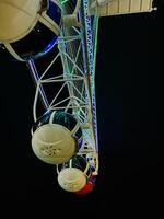 Low angle view of ferris wheel cabins illuminated with green, blue, and red neon lights at night against a dark sky, creating a vibrant and festive atmosphere perfect for travel and leisure themes photo
