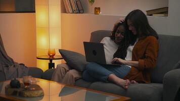 Warm and relaxed moment as a multiracial lesbian couple sits close together on the couch, enjoying each other's company while casually using a laptop in a peaceful home setting. video