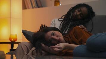 Dreamy moment between a multiracial lesbian couple - an African-American woman caresses her partner's head, then gazes upward with a gentle smile, lost in peaceful evening thoughts. video