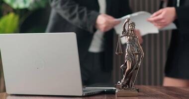 A laptop and a statue of justice against a background of business people shaking hands while discussing a course of action video