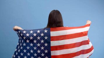 Young smiling happy woman holding american flag and looking to the camera isolated on blue color background. video