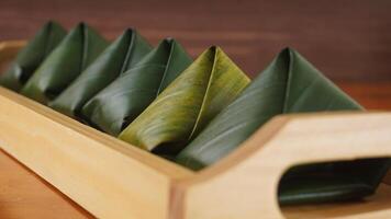 Selective focus of traditional Indonesian snack dessert wrap in green leaves called Kue Bugis on wooden tray photo
