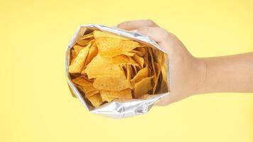 Man hand holds an opened foil bag of yellow nachos chips isolated on yellow background photo