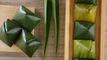Top view of Kue Bugis, popular traditional Indonesian snack dessert wrap in green leaves called on wooden background photo