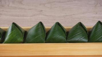 Close up focus of traditional Indonesian snack dessert wrap in green leaves called Kue Bugis on wooden tray photo