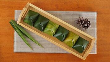 Top view of Kue Bugis, popular traditional Indonesian snack dessert wrap in green leaves called on wooden tray photo