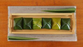 Top view of Kue Bugis, popular traditional dessert snack in Indonesian wrap in green leaves called on wooden tray photo