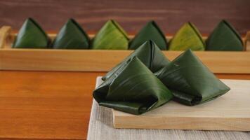 Selective focus of traditional Indonesian snack dessert wrap in green leaves called Kue Bugis on wooden platter photo