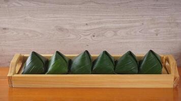 Traditional Indonesian snack dessert wrap in green leaves called Kue Bugis on wooden tray photo