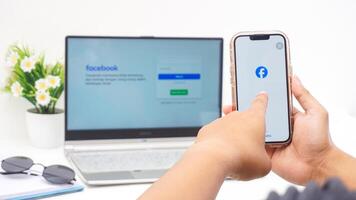 Yogyakarta, Indonesia, 2025 -Hand touching smartphone screen that shows front page of Facebook, social networking service application, isolated on white background photo