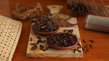 Dried cloves spice with dried leaves on wooden platters isolated on wooden texture background photo
