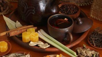 Wedang Uwuh on pottery tea cup with its composition that consist of sappan wood, cinnamon, ginger, lemongrass, and pala leaves, on pottery tray photo