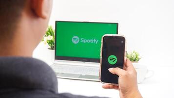 Yogyakarta, Indonesia, 2025 - Man holding smartphone that shows front page of Spotify, digital audio streaming platform application on the screen isolated on white background photo