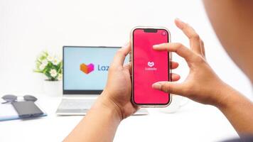 Yogyakarta, Indonesia, 2025 - Man touching smartphone screen that shows front page of Lazada e-commerce platform application isolated on white background photo