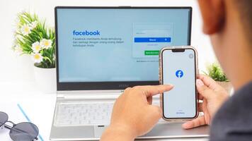 Yogyakarta, Indonesia, 2025 -Man using smartphone that shows front page of Facebook, social networking service application on the screen isolated on white background photo