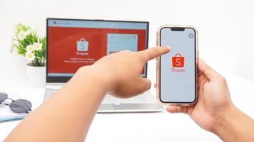 Yogyakarta, Indonesia, 2025 - Hand touching smartphone that shows front page of Shopee, e-commerce or online shopping platform application on the screen isolated on white background photo