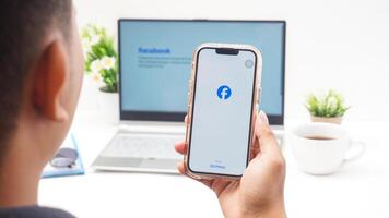 Yogyakarta, Indonesia, 2025 -Man holding smartphone with front page of Facebook, social networking service application on the screen isolated on white background photo