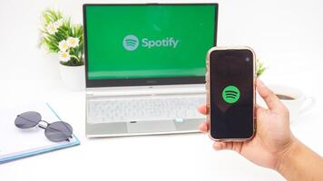 Yogyakarta, Indonesia, 2025 - Hand using smartphone that shows front page of Spotify, digital audio streaming platform application on the screen isolated on white background photo