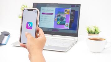 Yogyakarta, Indonesia, 2025 - Man hand using smartphone that shows front page of Picsart, a creative editing platform application on the screen isolated on white background photo