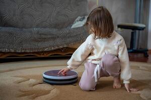 Little girl turning on a robot vacuum to clean the carpet at home. Concept of early tech interaction and smart home involvement. High quality photo