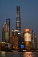 Shanghai, China - 1 April 2025 Evening skyline of Pudong district featuring illuminated Shanghai Tower, Shanghai World Financial Center, and Jin Mao Tower reflected in Huangpu River photo