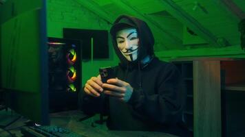 Lviv, Ukraine - June 03, 2024. Anonymous hacker smartphone monitor computer technology cyber crime thief masked man danger pointing finger no forbid warning scam fraud internet software attack virus video