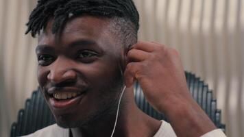 African American cyber man male guy smiling put on wired headphones enjoying listening to music good audio quality sound enjoy in earphones in white futurism studio indoors happy futuristic technology video