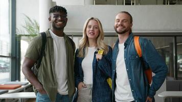 Group of diverse college friends standing together in university hallway smiling at camera cheerful students posing multicultural friendship Caucasian woman girl with African men guys in high school video