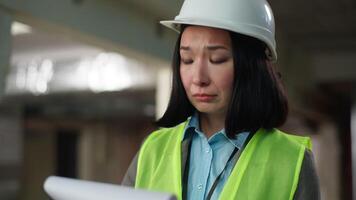 Upset confused Asian Korean Japanese woman in hard hat builder architect reading checking document paper problem loss building wrong plan construction project inspector engineer foreman chart failure video