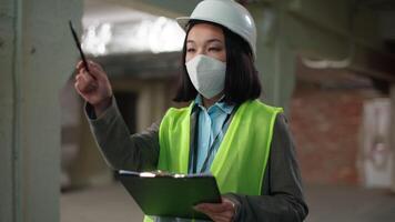 Asian Korean Chinese woman check building construction inspector in safety mask hard hat architect contractor developer writing checklist control female counting pointing girl builder foreman engineer video