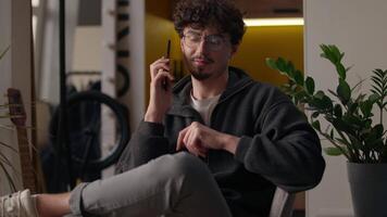 Happy Hispanic guy answering call using cellphone gadget connection at home male talking mobile phone remote conversation chatting man smiling indoors discussing news cheerful hipster calling friend video