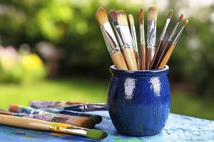 Abundance of Paintbrushes in a Blue Ceramic Pot on Painted Table in Garden Setting photo