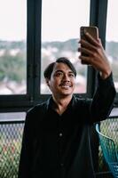 Happy young man taking selfie with smartphone near the window indoor photo