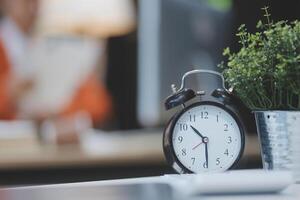 A clock is sitting on a desk in front of a plant photo