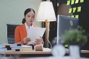 A woman in an orange jacket is reading a document photo