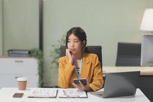 A woman sitting at a desk with a laptop and a cell phone photo