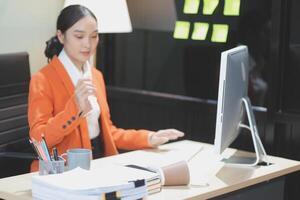 A woman in an orange jacket sitting at a desk with a computer photo