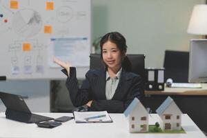 A woman sitting at a desk with a laptop and a house model photo